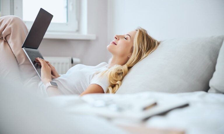 Mulher deitada em sua cama, com seu computador, bem relaxada e tranquila