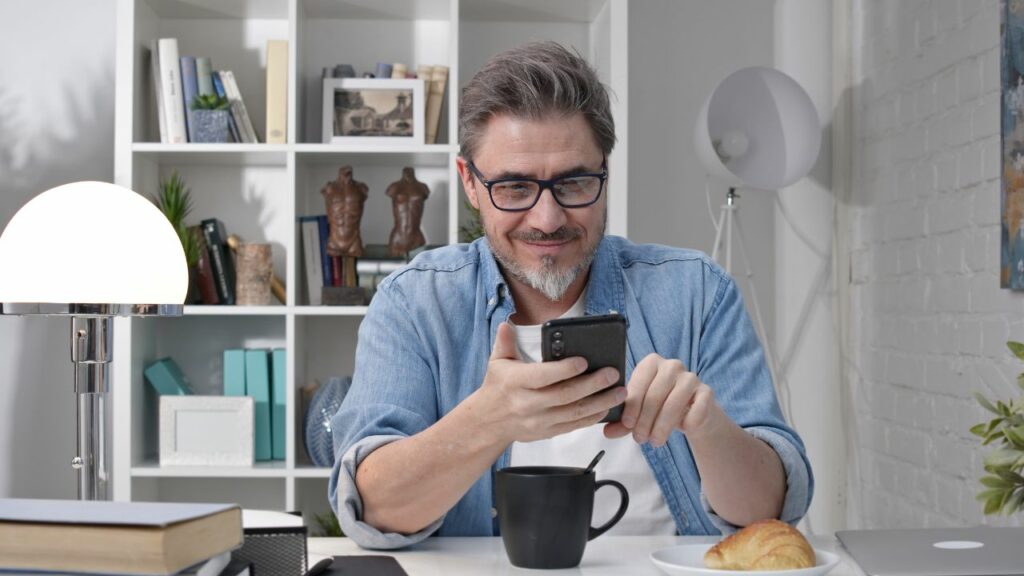 Homem usando o celular no café da manhã.